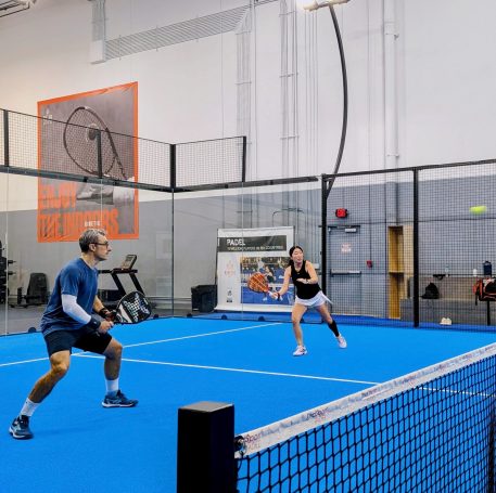 Left sided players: claim the middle of the court! A padel player moves from her left sided position to hit a forehand volley while her partner prepares for their opponent's return shot.