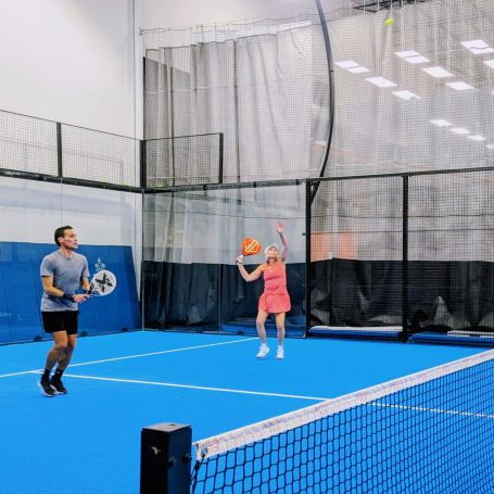 "I go!" A padel player prepares for an overhead smash as her partner keeps an eye on the opponents
