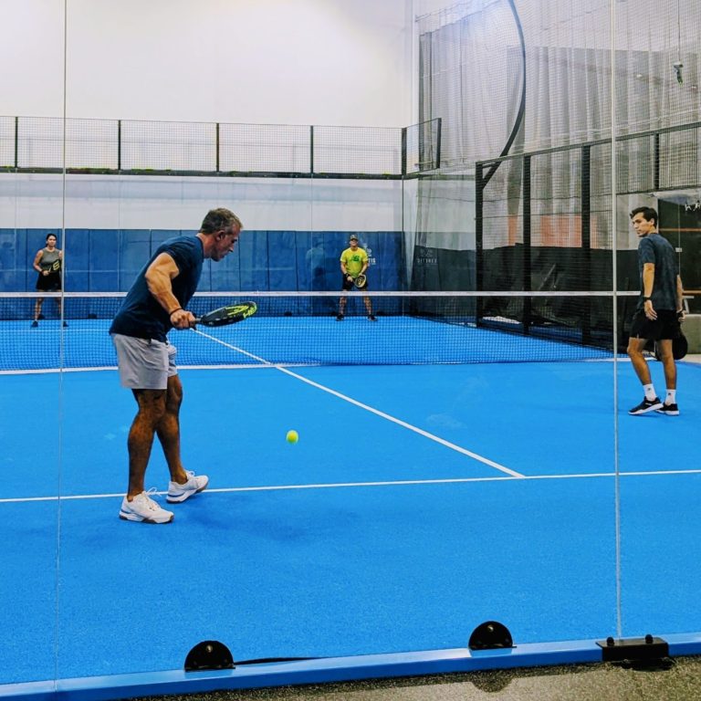Group Clinics A padel player prepares to serve to his opponents during a clinic session while his partner looks on.