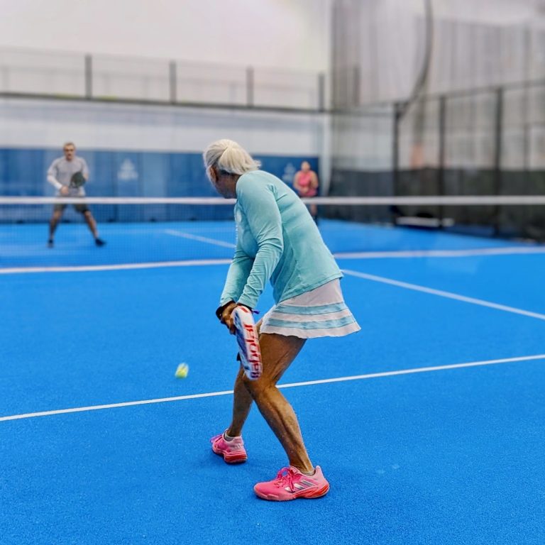 Personalized Coaching Sessions A padel player prepares to hit a backhand return of serve as two opponents across the net ready themselves for the shot.